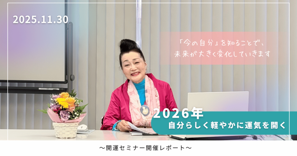 セミナー会場でピンクのジャケットを着た女性が机に座り、花かごとノートパソコンが置かれている様子。背景には縦型ブラインドとスクリーンがあり、セミナーの開催日とメッセージが表示されている。